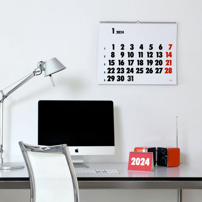 partial view of modern desk setup with computer and minimalist wall calendar in black, white, and red on wall