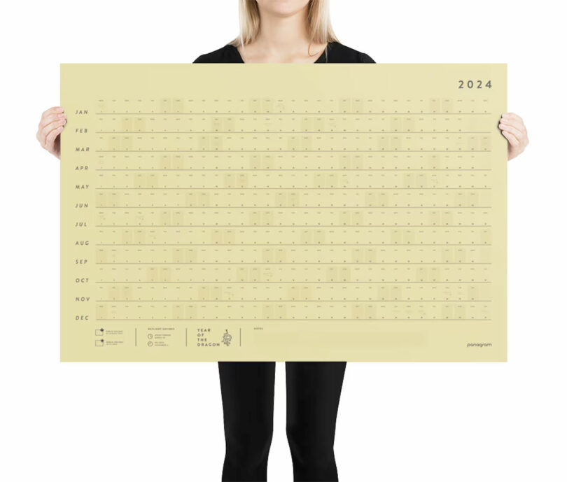 woman in black hold large gold wall calendar out in front of her
