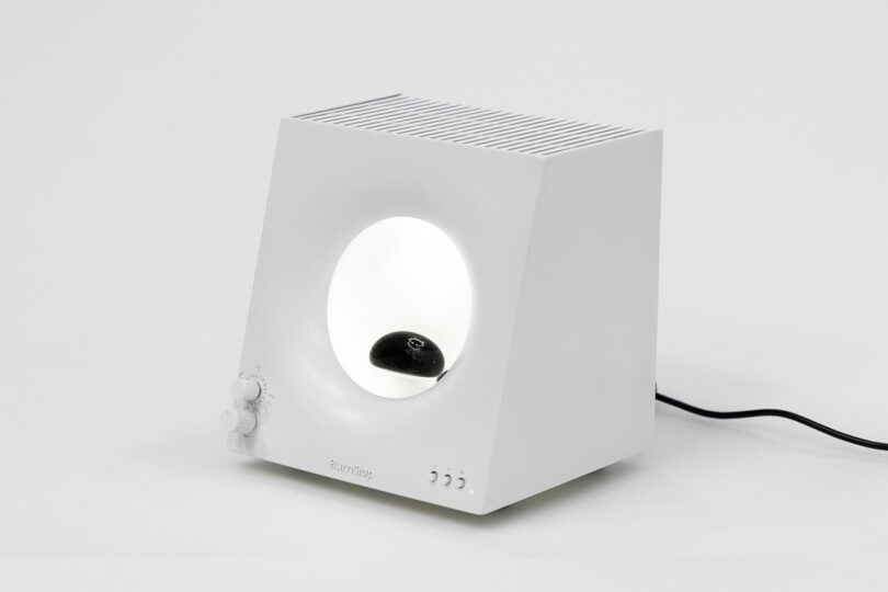 Small square-shaped white audio device with small circular window containing a globule of nanoscale ferromagnetic particles designed to move in relation to music.