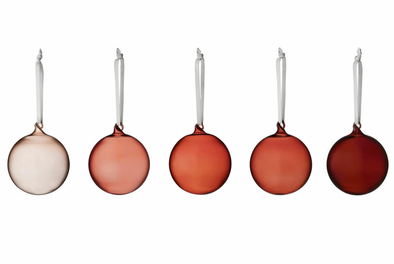 fine tonal glass ball ornaments in shades of pink and red hanging in front of white background