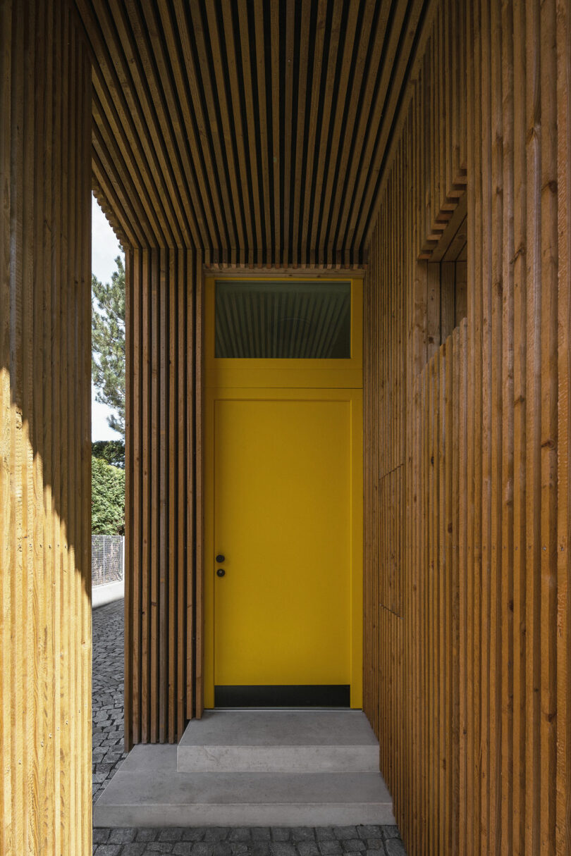 view into covered entryway into modern house clad in wood slats with yellow door