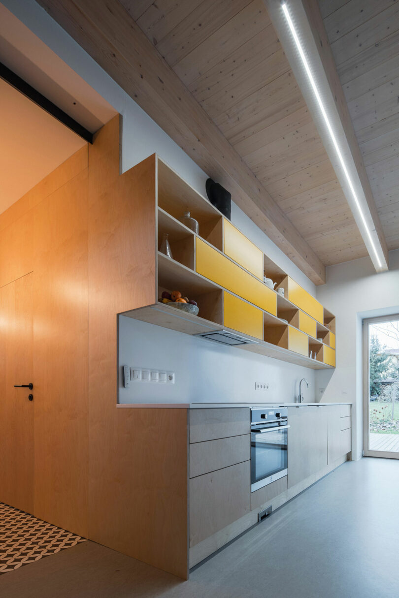 long interior view of modern minimalist kitchen with wood and yellow cabinets to left