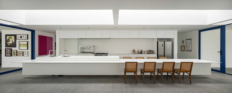 interior view of minimalist white kitchen with long island and wood chairs