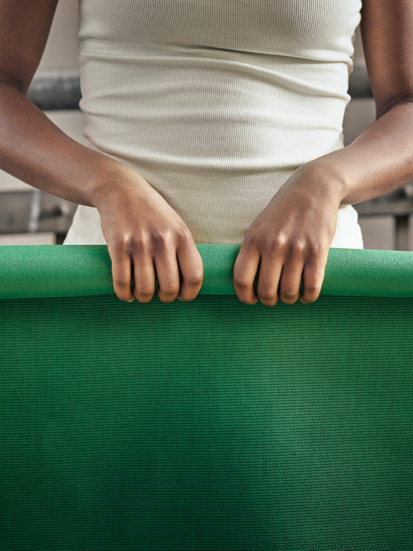 partial torso view of person in white tank rolling up dark green yoga mat
