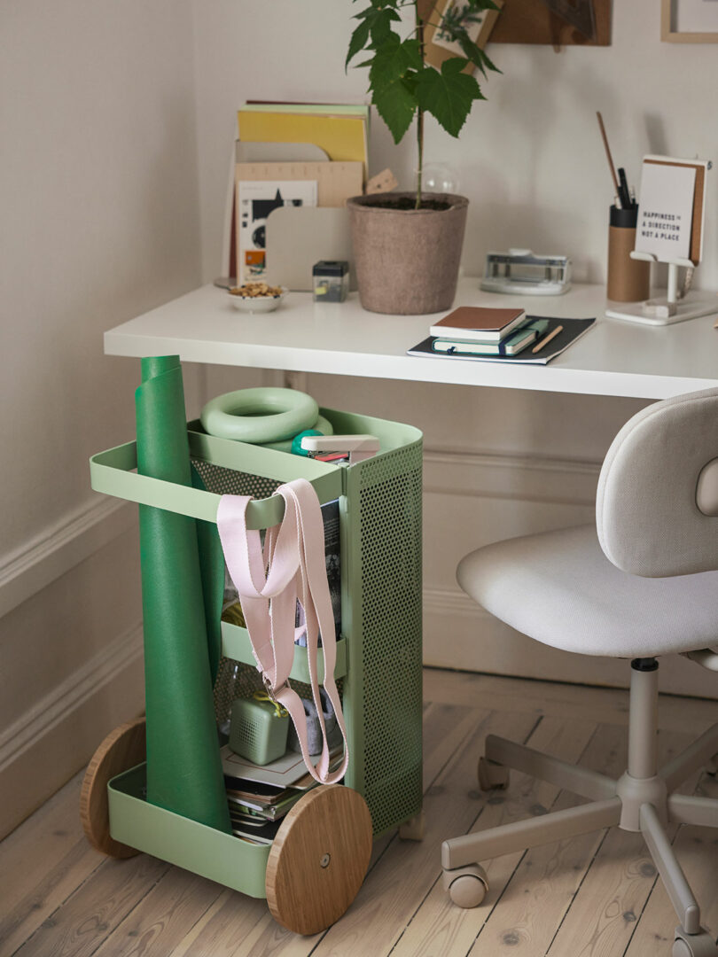 Angled corner of a room with desk setup with light green rolling cart holding fitness gear in front