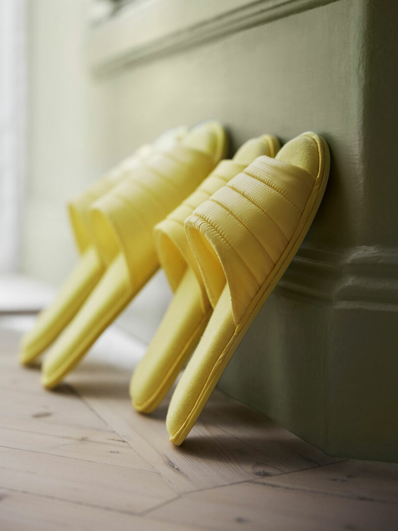 two pairs of light yellow slippers propped up on a wall