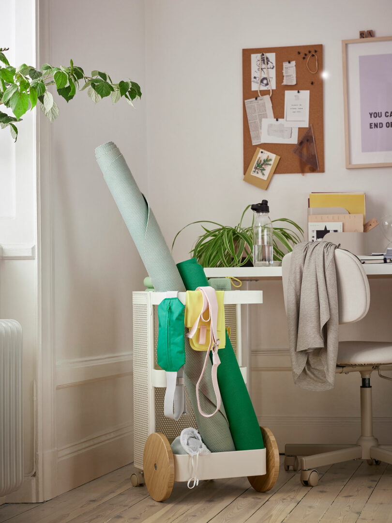 Angled corner of a room with desk setup with white rolling cart holding fitness gear in front