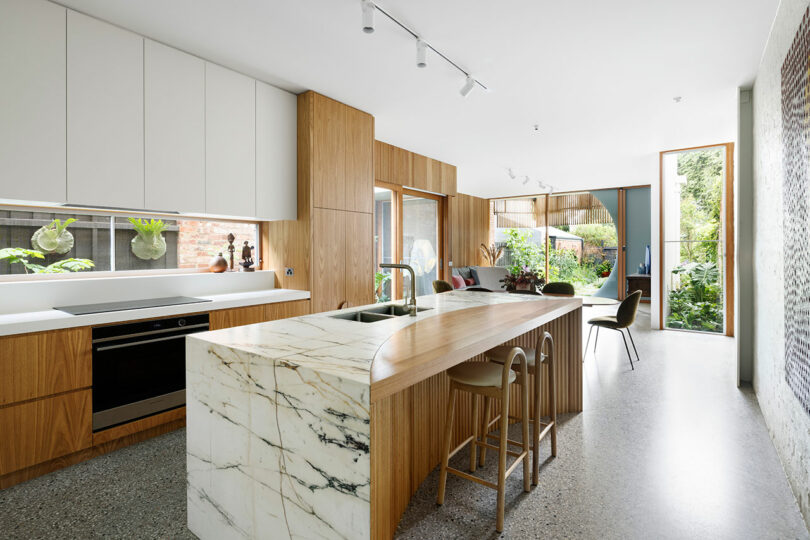 angled view of modern kitchen with grained black and white marble countertops and wood slatted cabinets