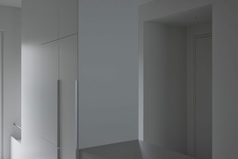 angled view of minimalist white kitchen and built-in fridge